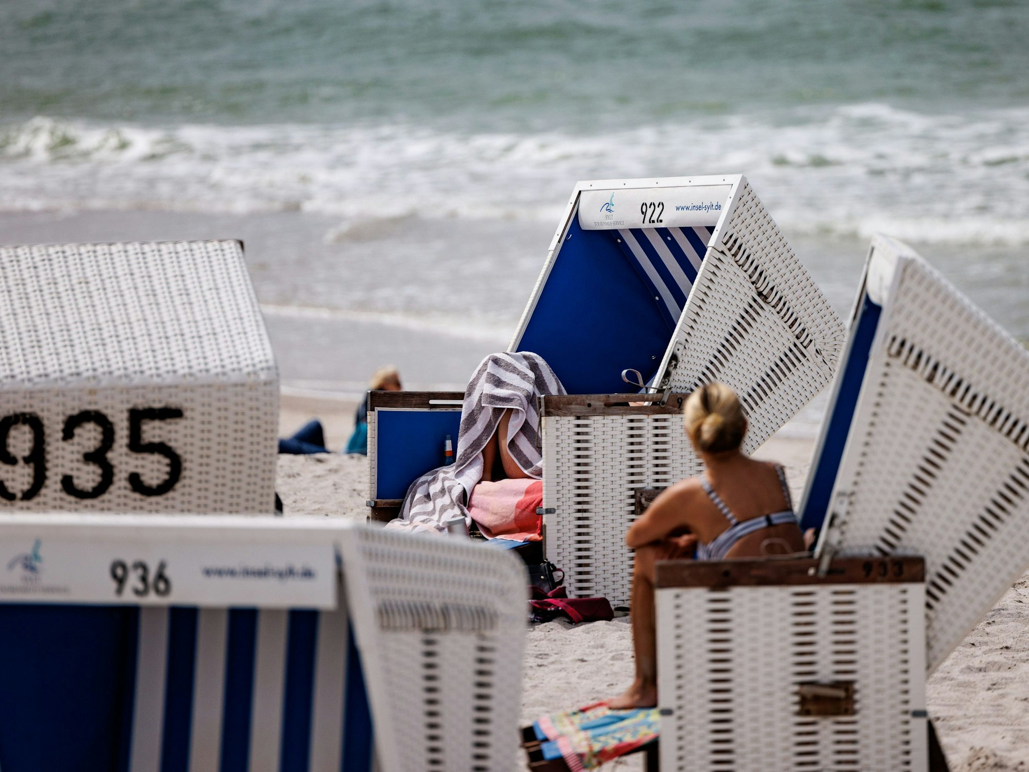 Das Foto aus dem Jahr 2022 zeigt mehrere weiß-blaue Strandkörbe am Sylter Strand. Im Hintergrund schlagen Wellen der Nordsee ans Ufer.