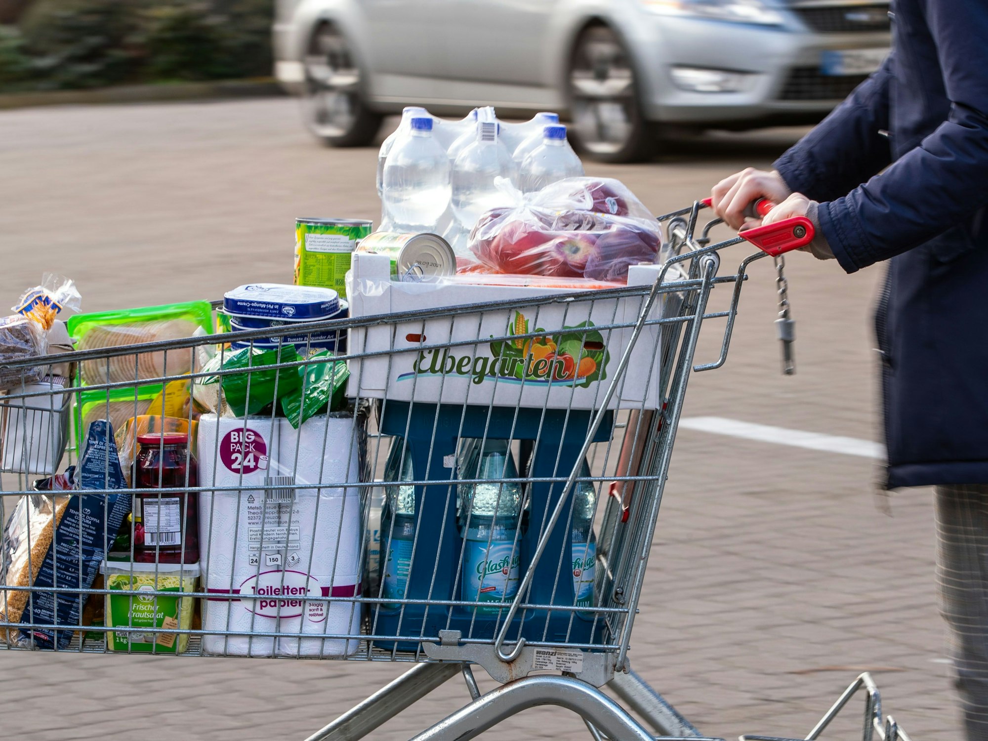 Auf dem Bild sehen sie einen mit Lebensmitteln gefüllten Einkaufswagen auf einem Supermarktparkplatz.