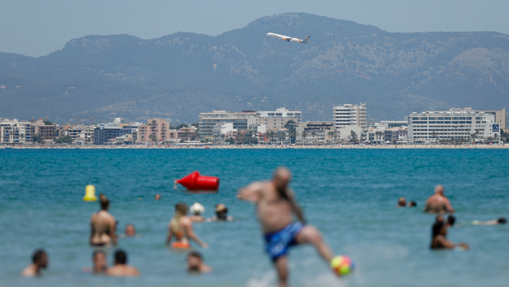 Ein Flugzeug fliegt über das Meer, während Urlauber im Wasser baden.