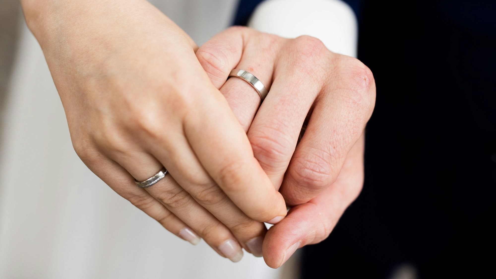 Eine Frauen- und eine Männerhand mit silbernen Eheringen.