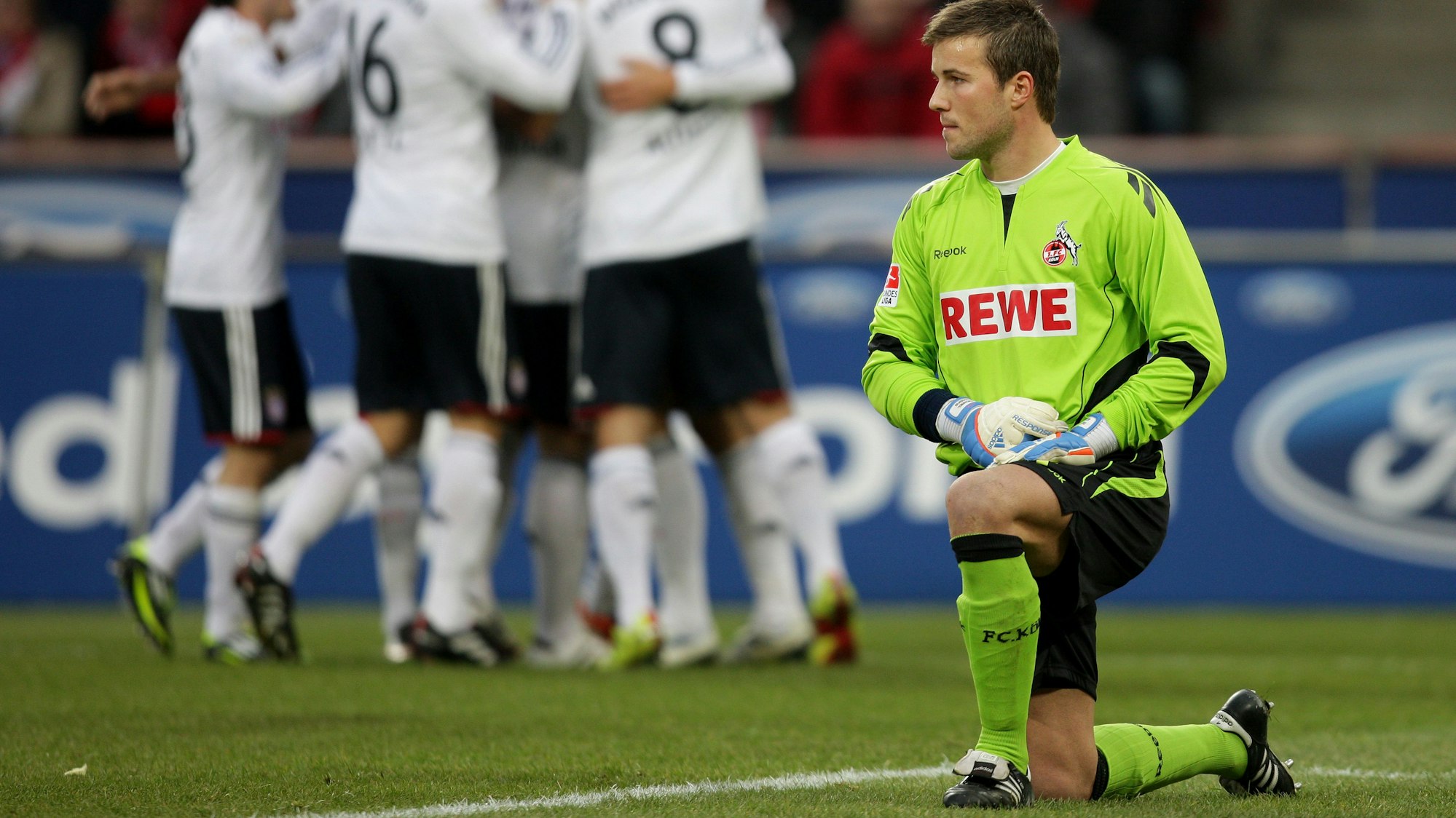 Kölns Torwart Michael Rensing (r) kniet auf dem Boden, während die Münchener im Hintergrund ein Tor feiern.