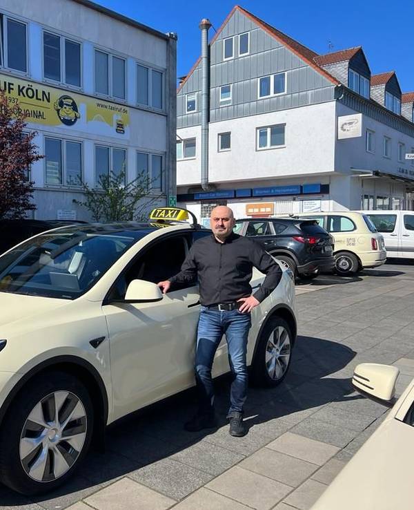 Ein Taxi-Fahrer steht neben seinem Auto.