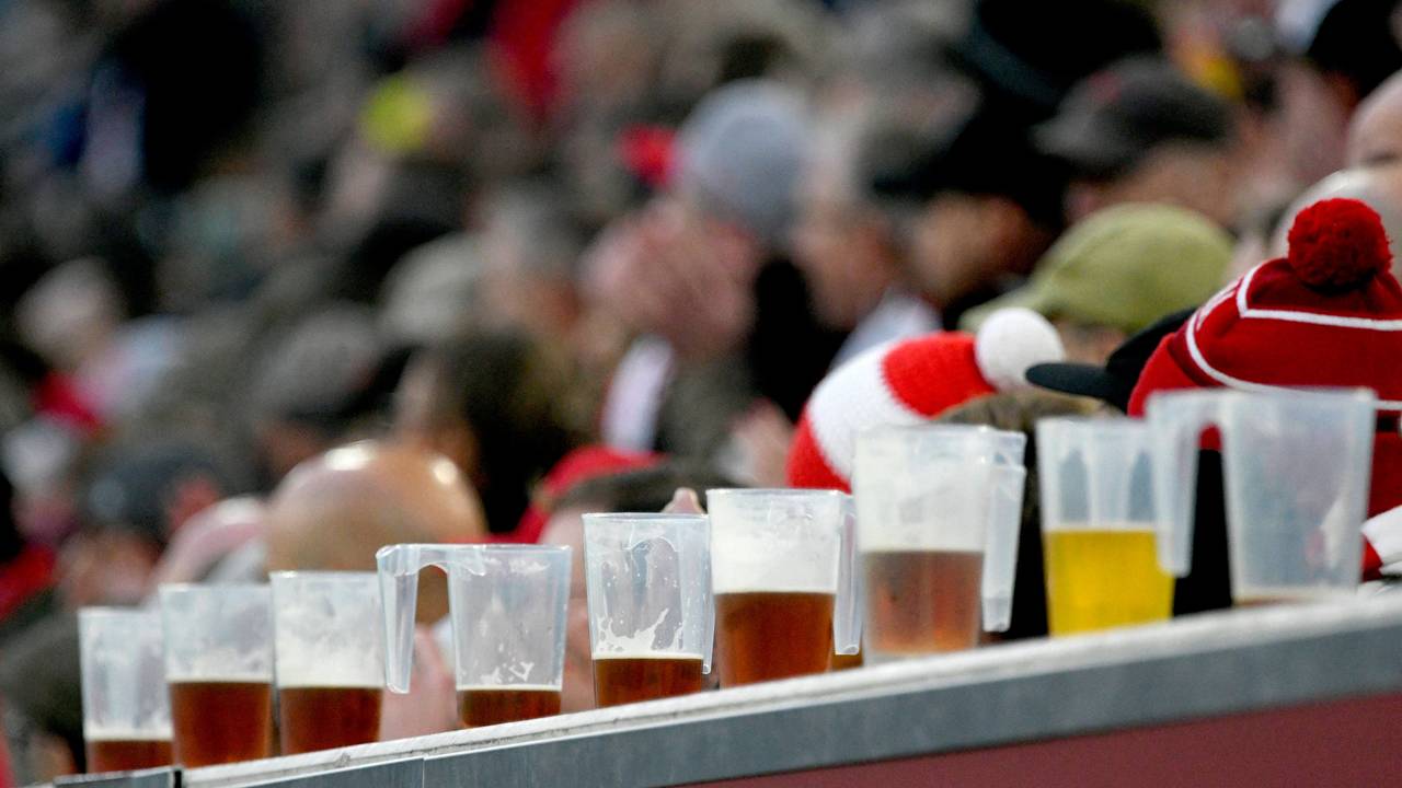 Halb gefüllte Bierbecher aus Plastik stehen aufgereiht auf einer Bande vor den Zuschauern.