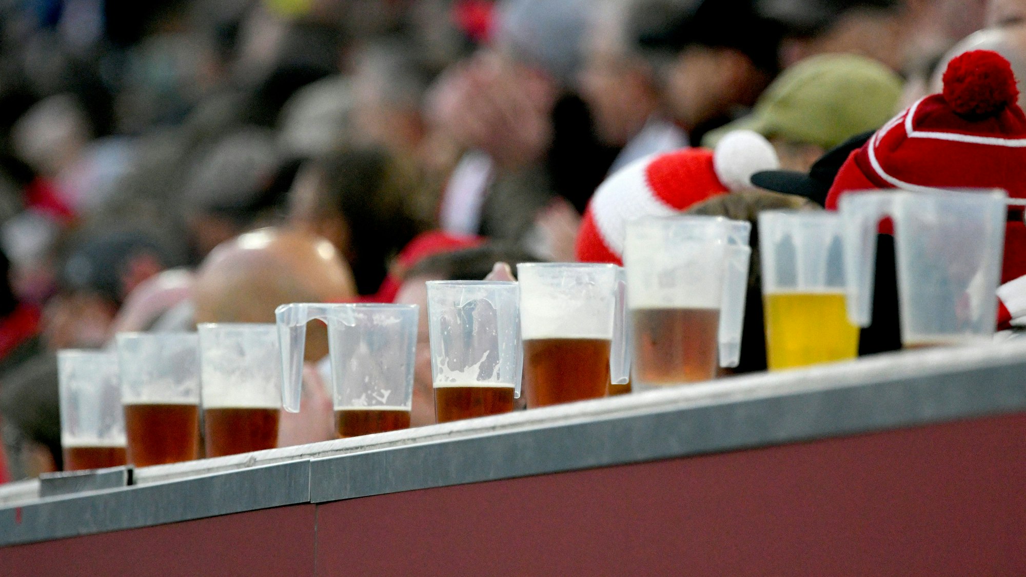 Halb gefüllte Bierbecher aus Plastik stehen aufgereiht auf einer Bande vor den Zuschauern.