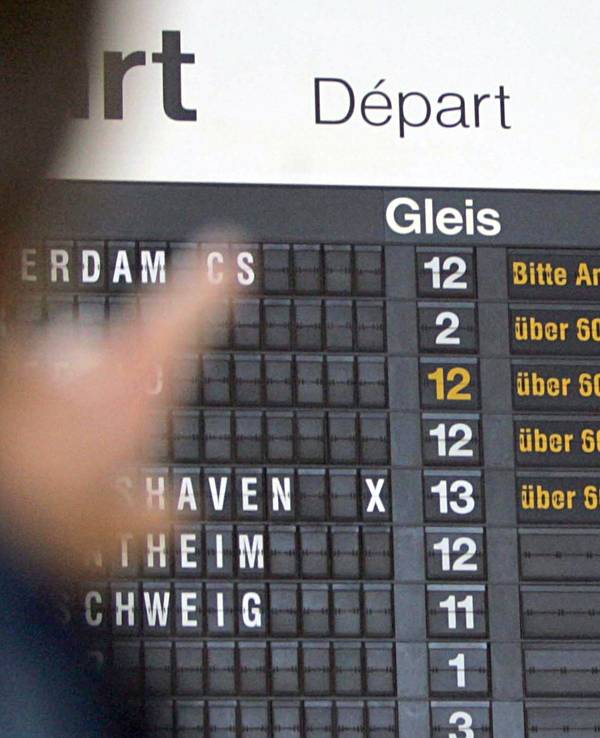 Auf dem Foto zu sehen, eine reisende Person vor einer Anzeigetafel der Deutschen Bahn. Diese zeigt für jeden Zug eine Verspätung von 60 Minuten an.