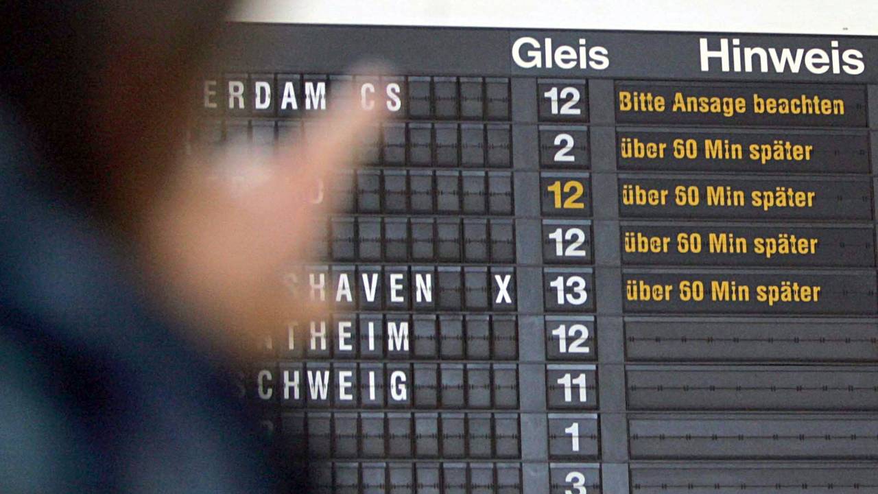 Auf dem Foto zu sehen, eine reisende Person vor einer Anzeigetafel der Deutschen Bahn. Diese zeigt für jeden Zug eine Verspätung von 60 Minuten an.