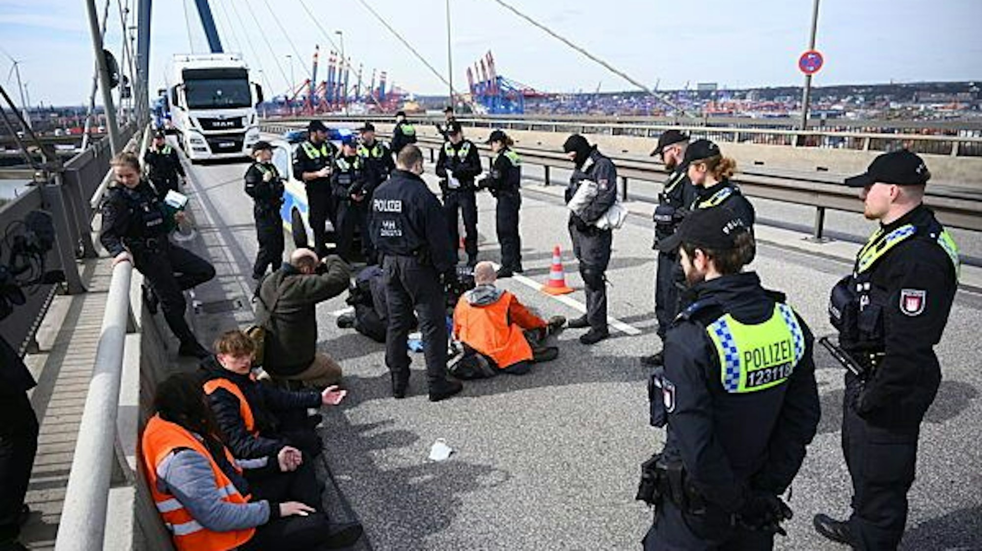 Polizisten stehen und arbeiten um einen auf der Fahrbahn festgeklebten Klimaaktivisten. Mehrere Klimaaktivisten haben den Verkehr auf der Hamburger Köhlbrandbrücke blockiert.