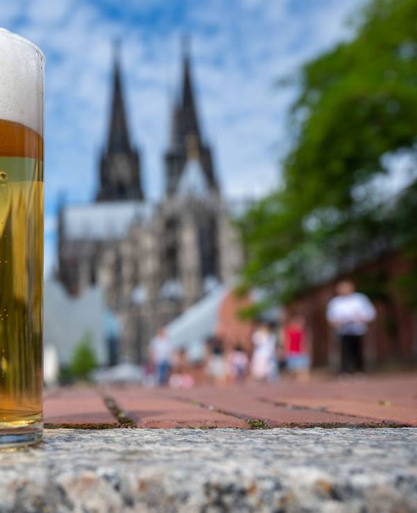 Zwei Kölsch-Gläser stehen auf einer Mauer, im Hintergrund ist der Dom zu sehen.
