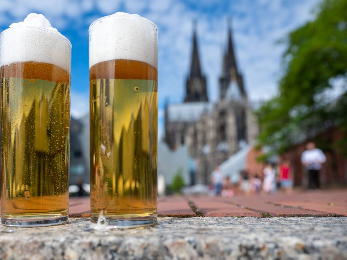 Zwei Kölsch-Gläser stehen auf einer Mauer, im Hintergrund ist der Dom zu sehen.