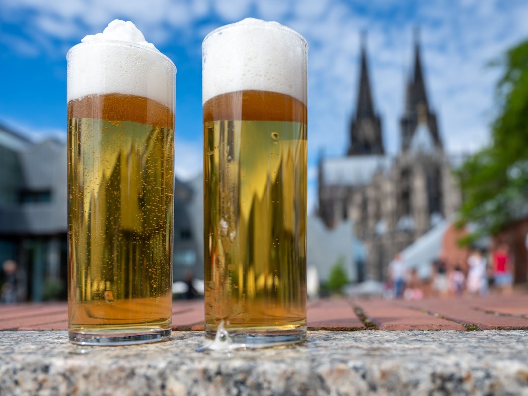 Zwei Kölsch-Gläser stehen auf einer Mauer, im Hintergrund ist der Dom zu sehen.