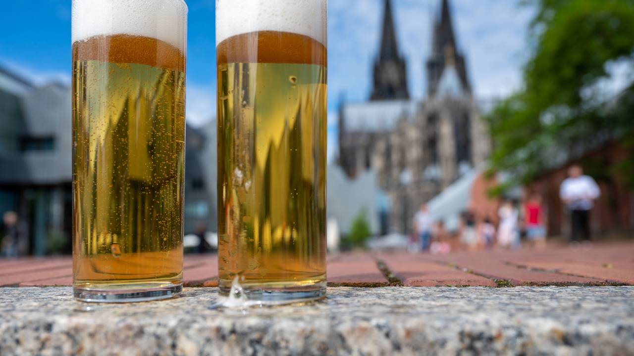 Zwei Kölsch-Gläser stehen auf einer Mauer, im Hintergrund ist der Dom zu sehen.
