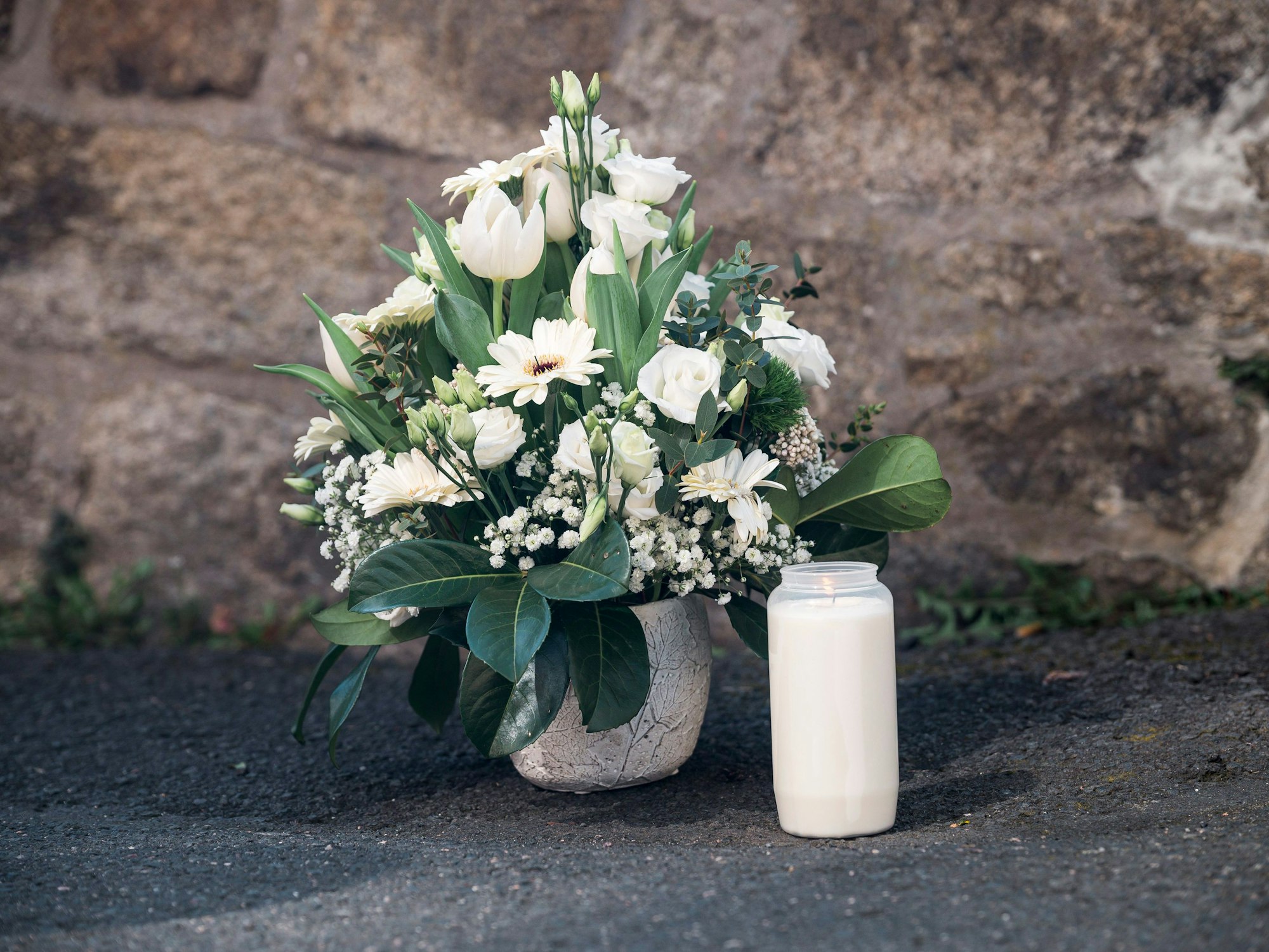 Auf dem Bild sieht man einen Blumenstrauß und eine Kerze vor einer Mauer. Hinter der Mauer liegt ein Kinderheim, wo ein zehnjähriges Mädchen getötet worden ist.
