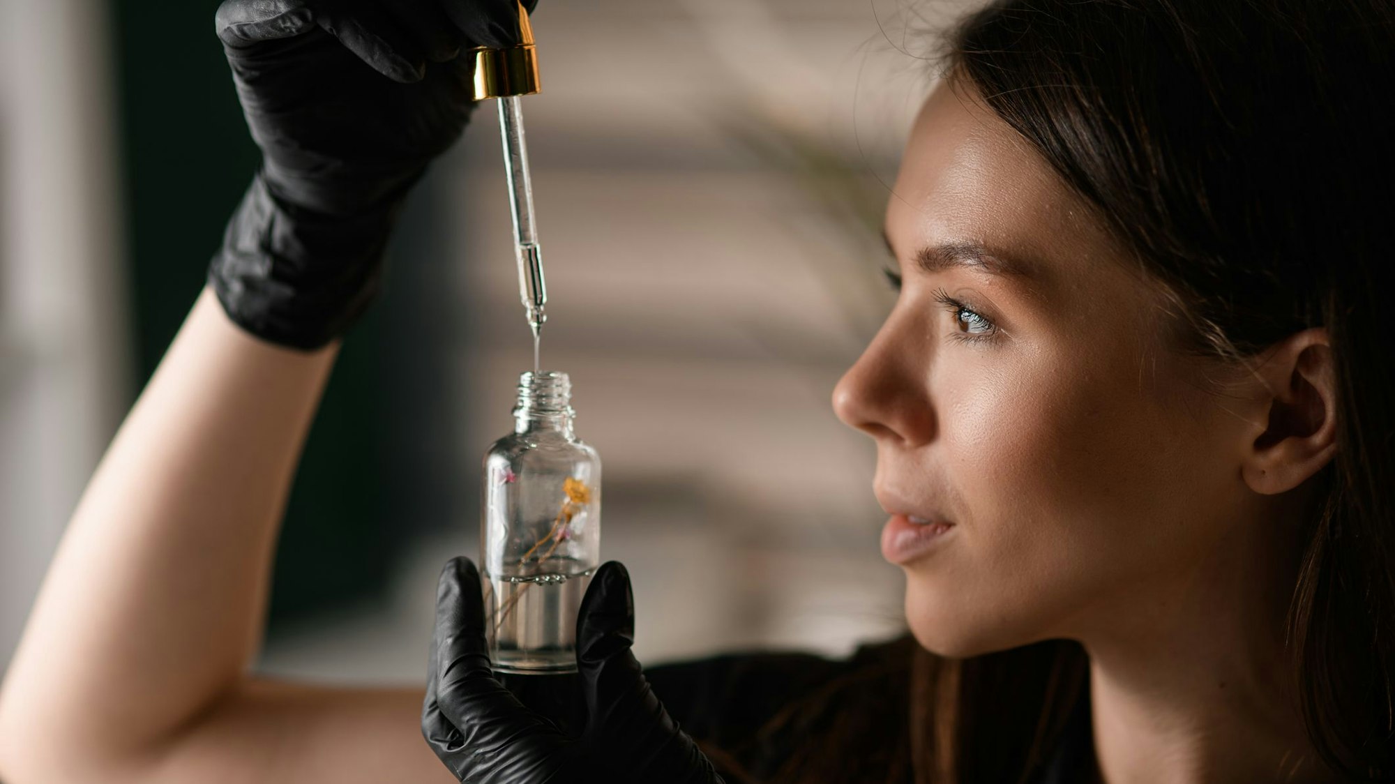 Eine junge Frau holt mit einer Pipette eine kosmetische Flüssigkeit aus einem Flakon.