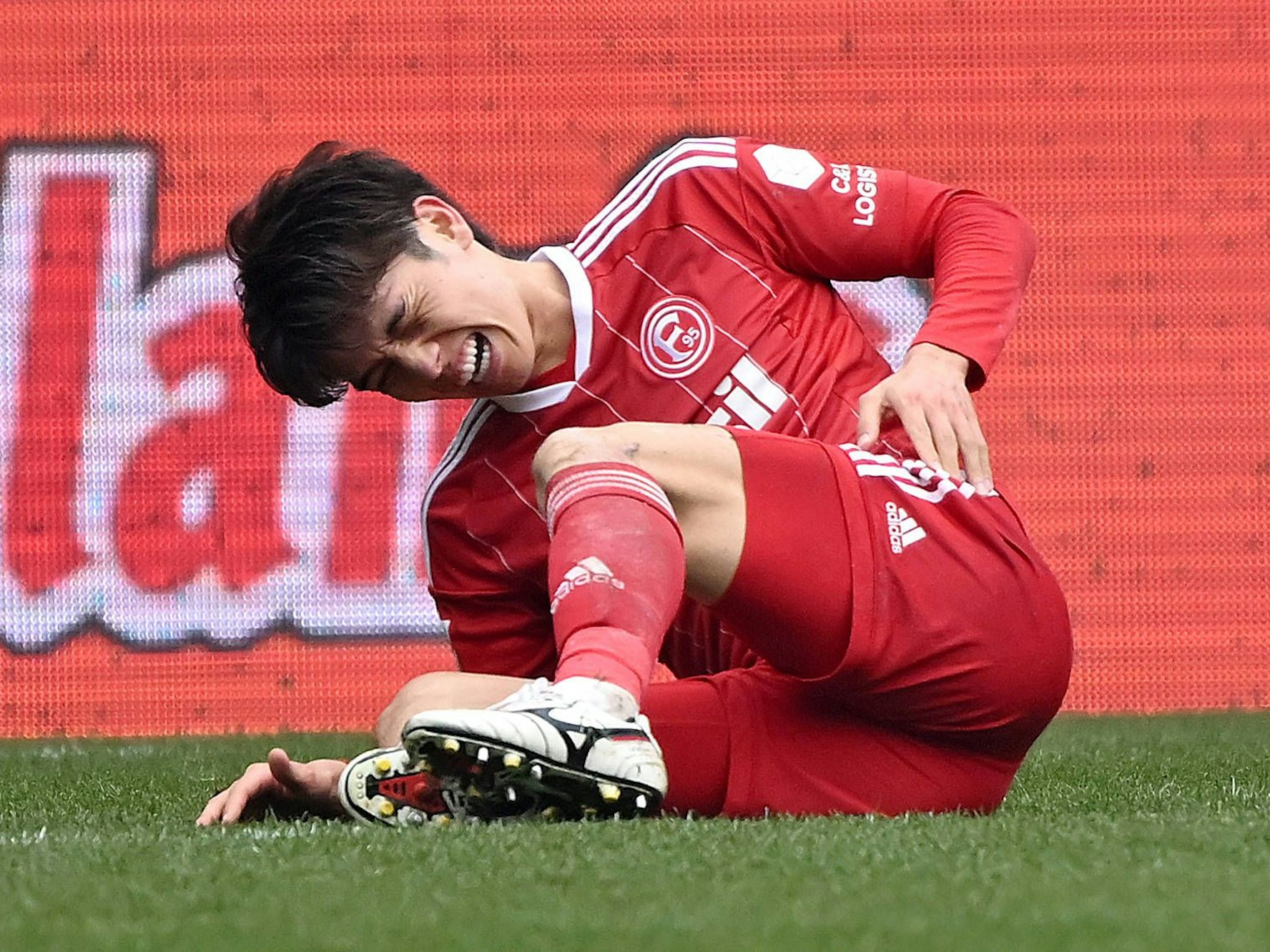 Ao Tanaka sitzt auf dem Rasen und hält sich die Hüfte.