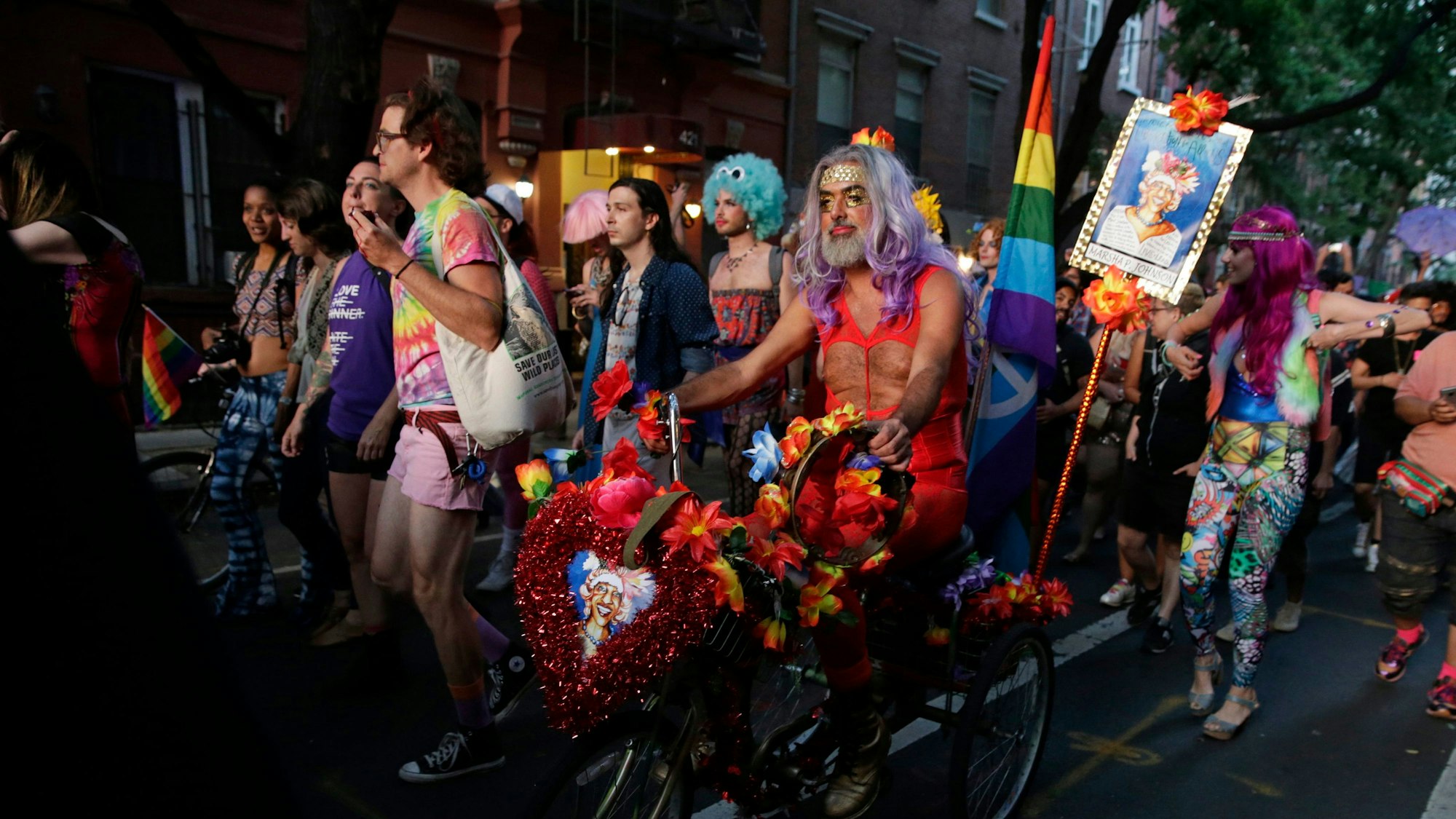Menschen ziehen mit Regenbogenfahnen durch die Straßen.