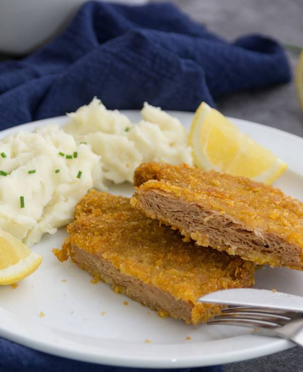 Auf dem Foto sieht man ein veganes Schnitzel auf einem Teller, zusammen mit Kartoffelpüree und einer Zitrone.