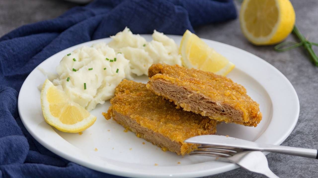Auf dem Foto sieht man ein veganes Schnitzel auf einem Teller, zusammen mit Kartoffelpüree und einer Zitrone.