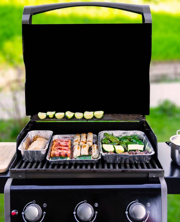 Auf dem Foto sieht man einen offenen Gasgrill, auf dem Fleisch und Gemüse gegrillt wird.