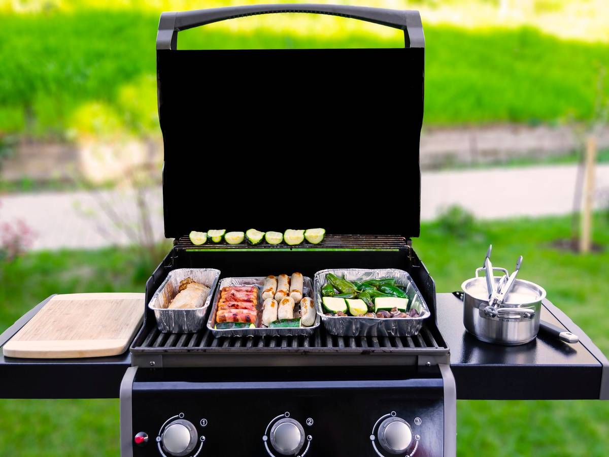 Auf dem Foto sieht man einen offenen Gasgrill, auf dem Fleisch und Gemüse gegrillt wird.