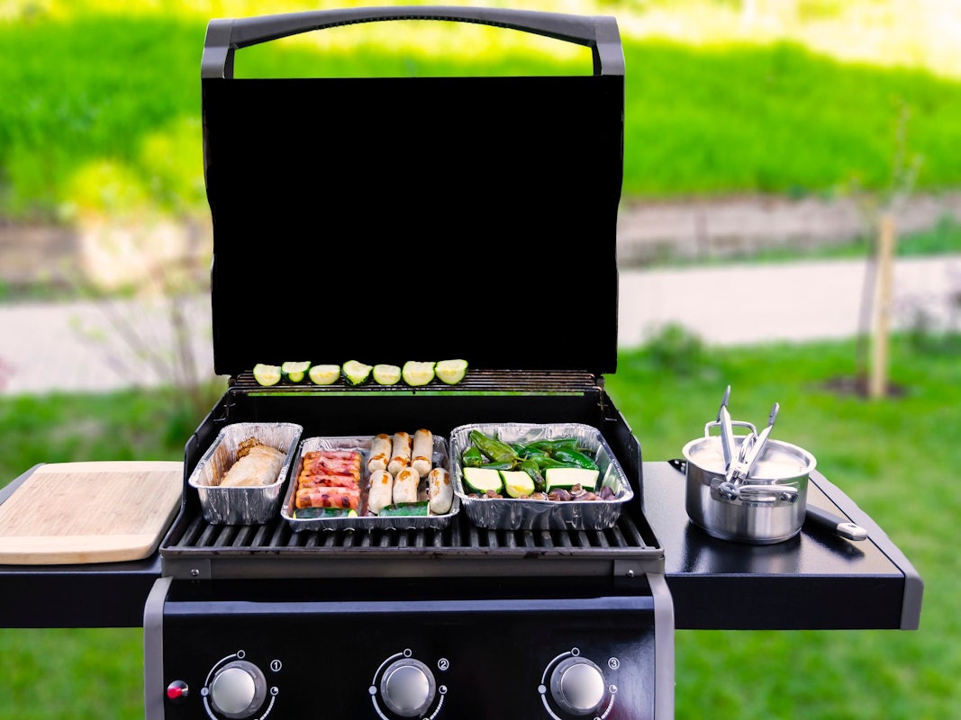 Auf dem Foto sieht man einen offenen Gasgrill, auf dem Fleisch und Gemüse gegrillt wird.