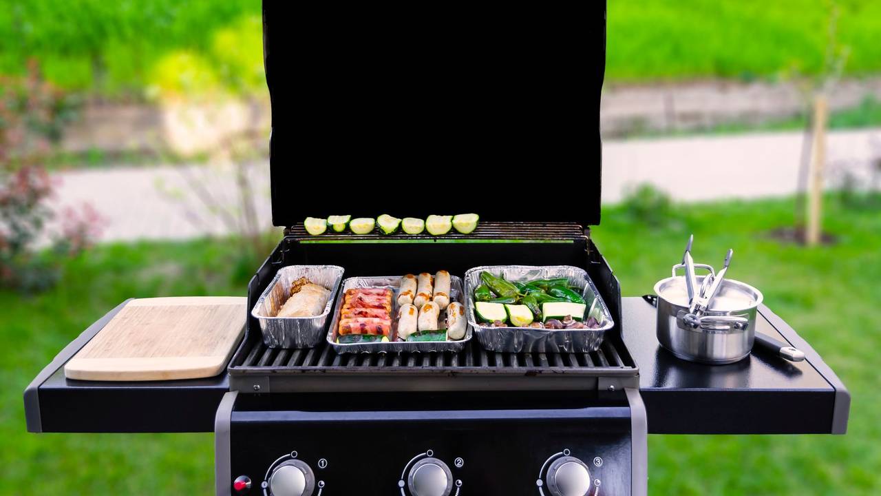 Auf dem Foto sieht man einen offenen Gasgrill, auf dem Fleisch und Gemüse gegrillt wird.