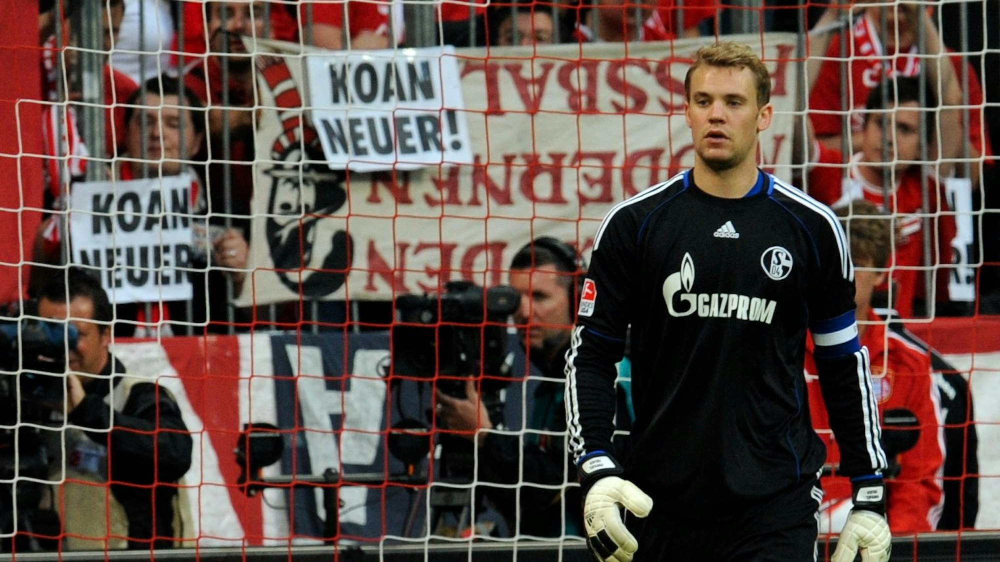 Hinter dem Torhüter von Schalke, Manuel Neuer, halten Bayern-Fans Zettel mit der Aufschrift „Koan Neuer!“ in die Höhe.