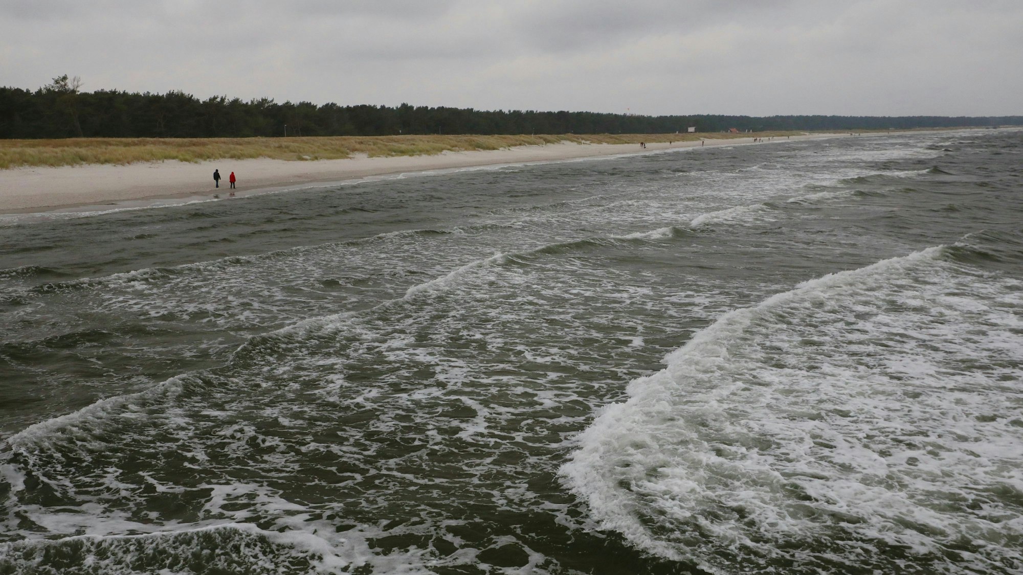 Zwei Spaziergänger gehen am Strand von Prerow entlang.