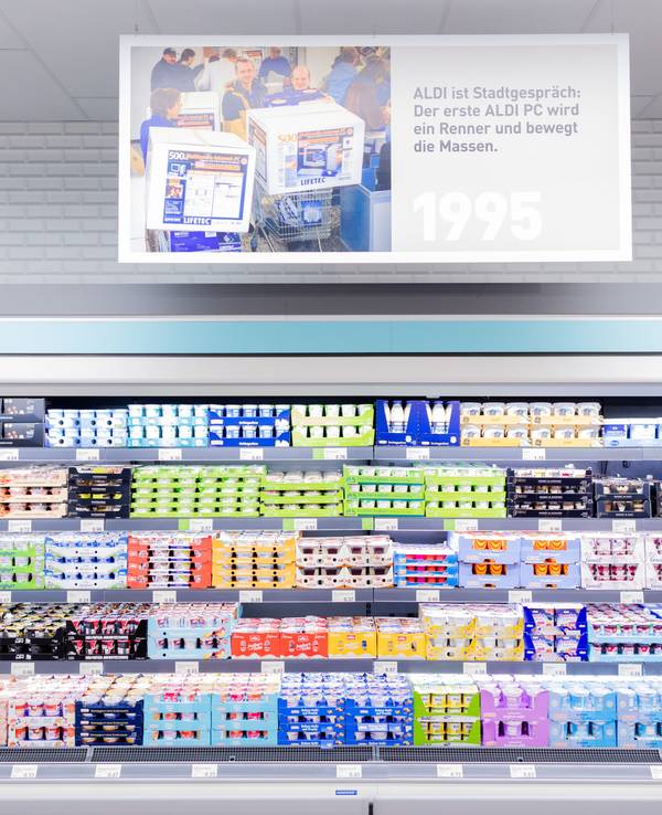 Schilder mit historischen Motiven hängen über einem Regal mit Molkereiprodukten im "neuen ältesten Aldi Markt".
