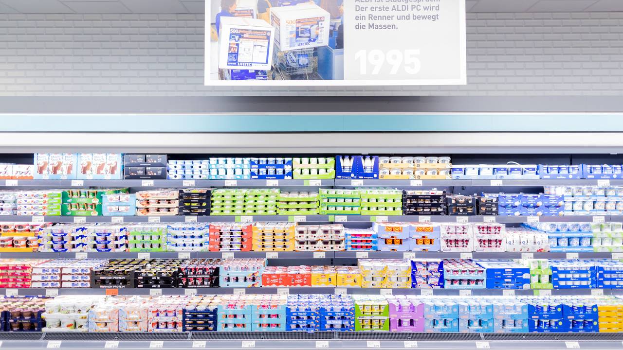 Schilder mit historischen Motiven hängen über einem Regal mit Molkereiprodukten im "neuen ältesten Aldi Markt".