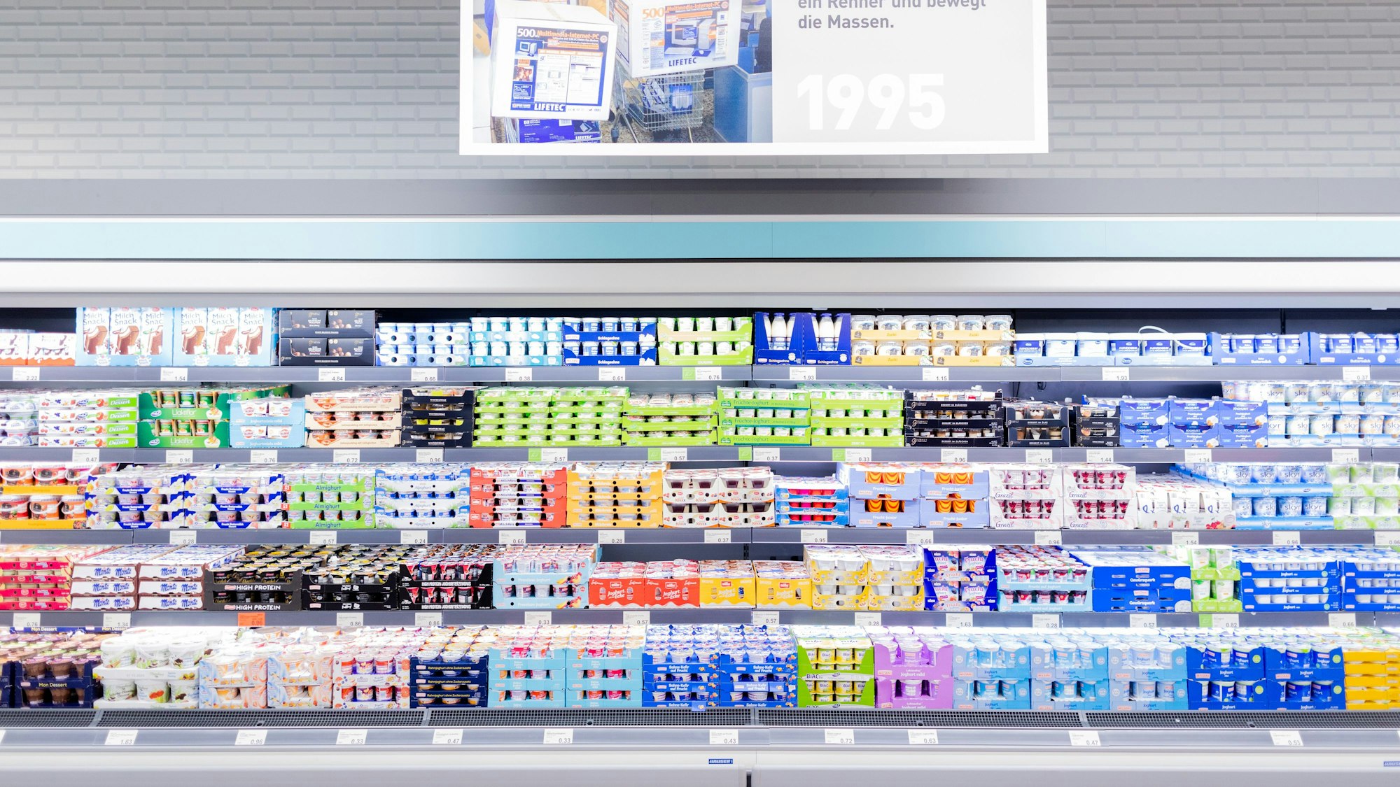 Schilder mit historischen Motiven hängen über einem Regal mit Molkereiprodukten im "neuen ältesten Aldi Markt".