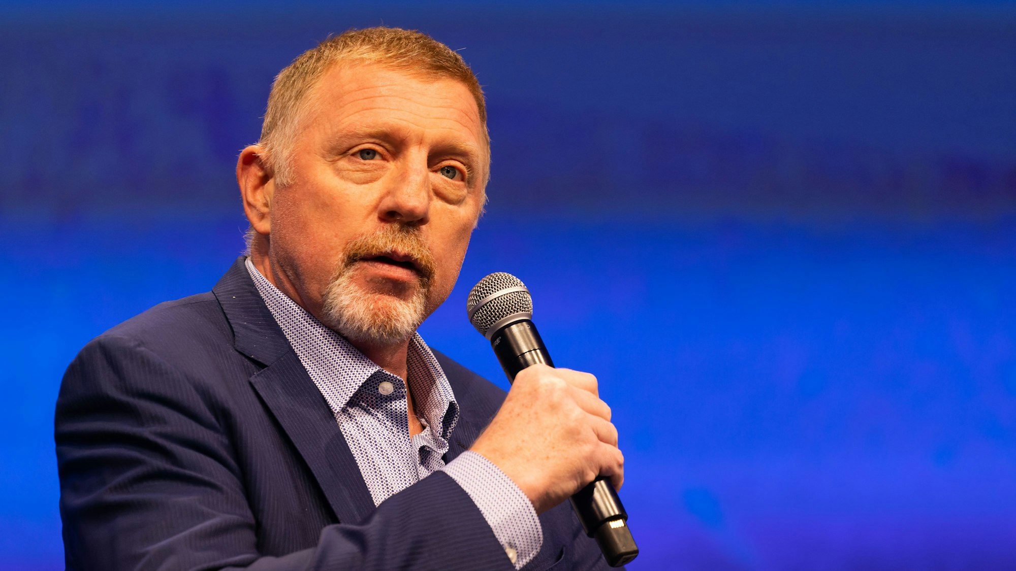Boris Becker hat ein Mikrofon in der Hand.