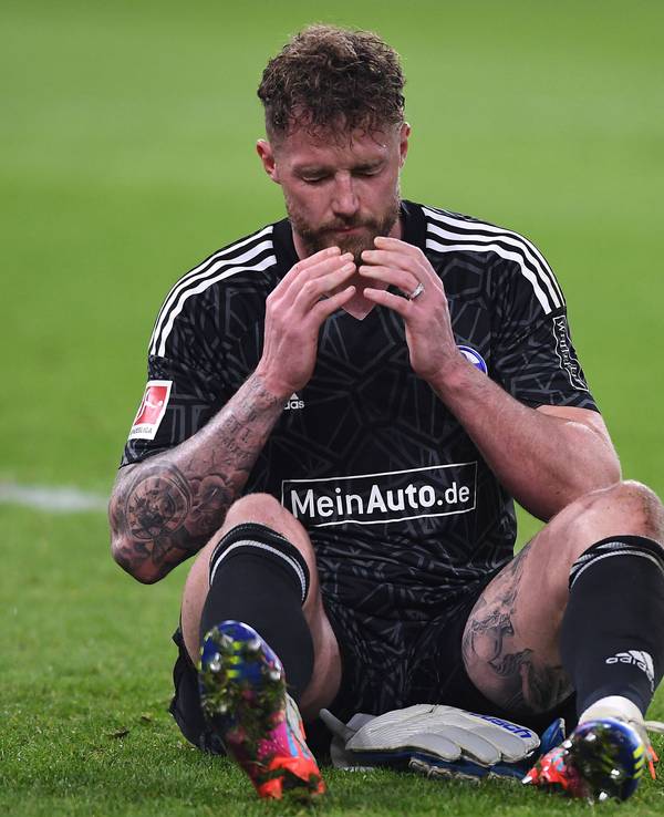 Ralf Fährmann sitzt in der Veltins Arena auf dem Rasen und schlägt die Hände vor sein Gesicht.