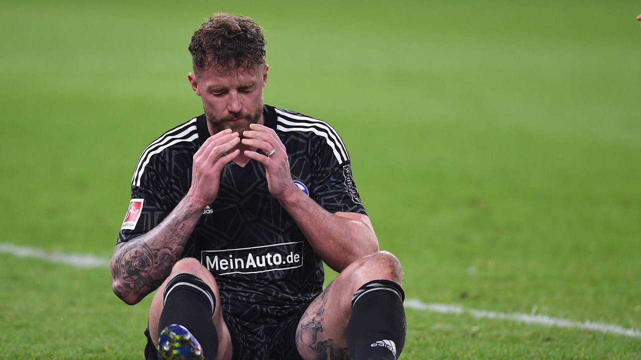 Ralf Fährmann sitzt in der Veltins Arena auf dem Rasen und schlägt die Hände vor sein Gesicht.