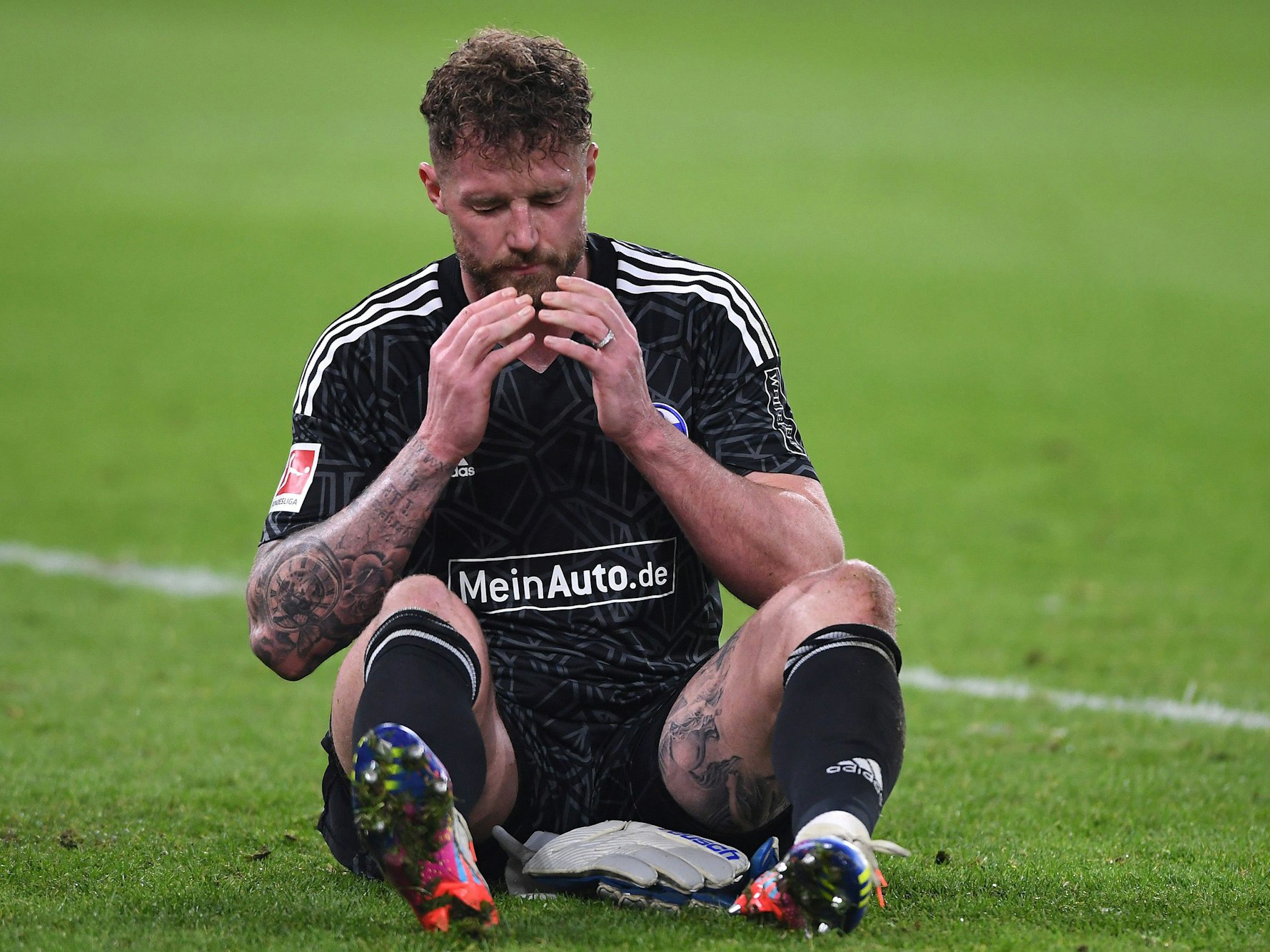 Ralf Fährmann sitzt in der Veltins Arena auf dem Rasen und schlägt die Hände vor sein Gesicht.