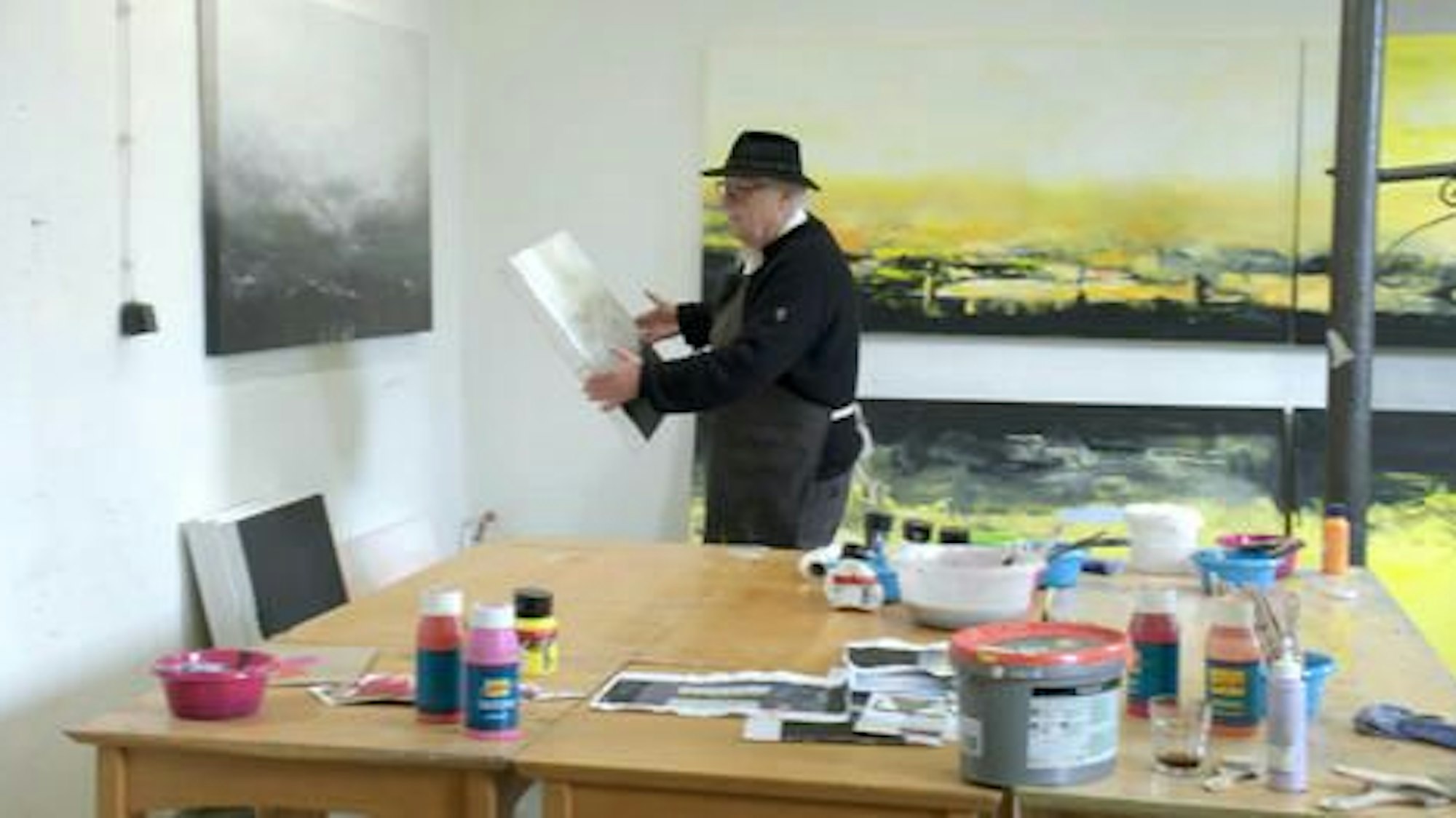 Helge Achenbach hält eine Leinwand in der Hand.