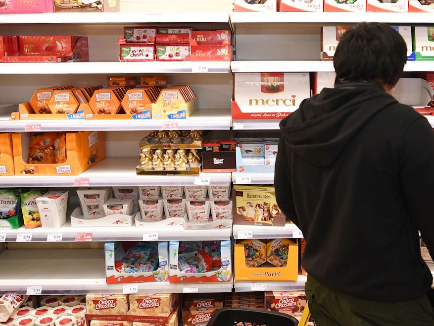 Ein Mann steht in einem Supermarkt vor einem Regal mit verschiedenen Schokoladen.