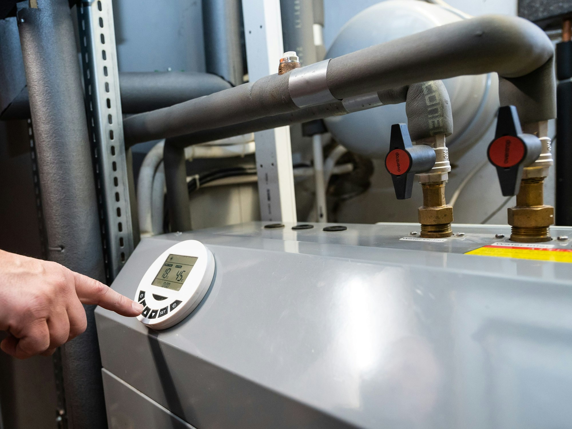 Ein Mann bedient eine Luftwärmepumpe, die im Keller eines Wohnhauses steht.