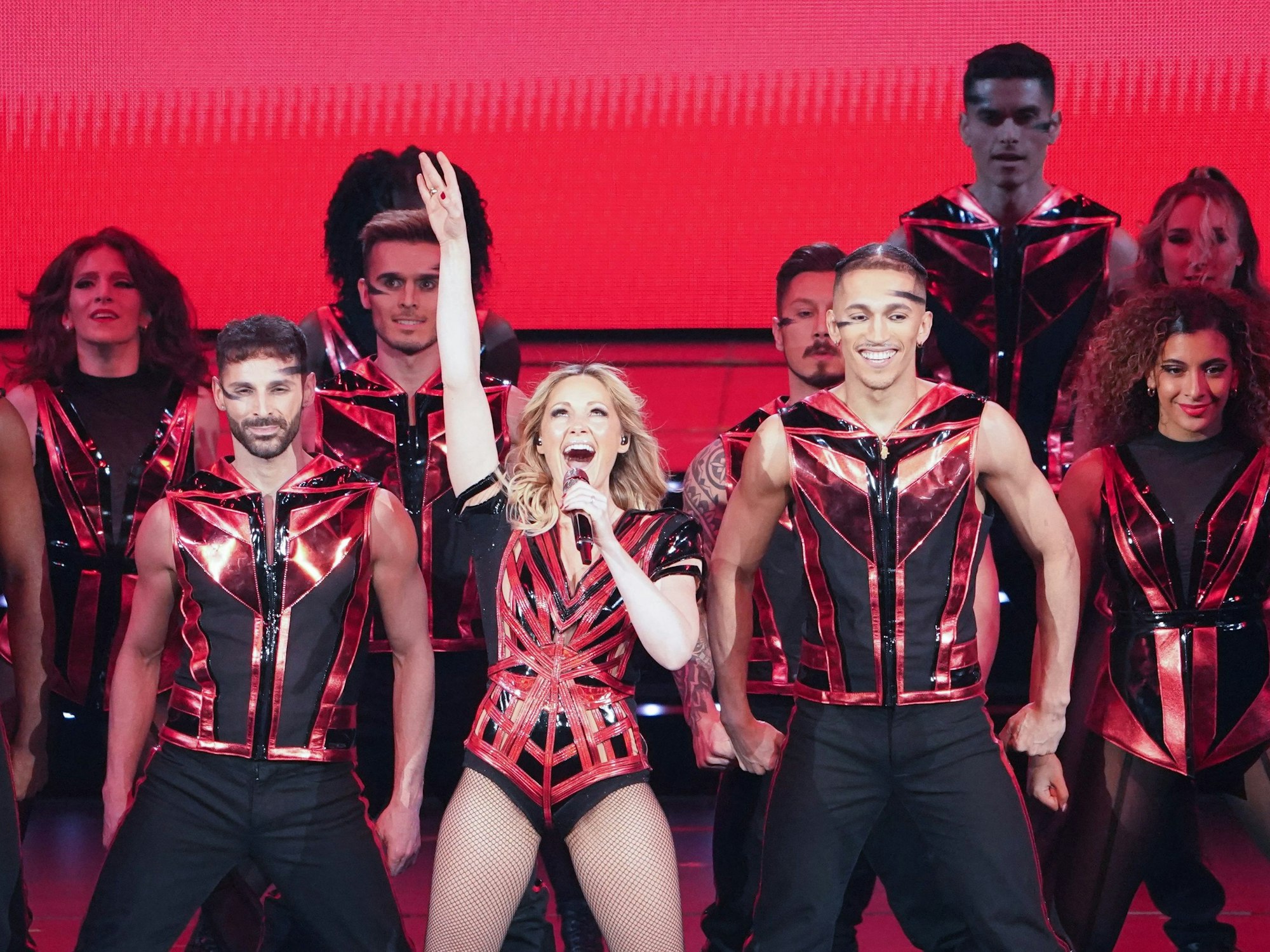 Hier zu sehen, Helene Fischer in einem schwarz-roten Kostüm zusammen mit ihren Tänzerinnen und Tänzern auf der Bühne in Hamburg.