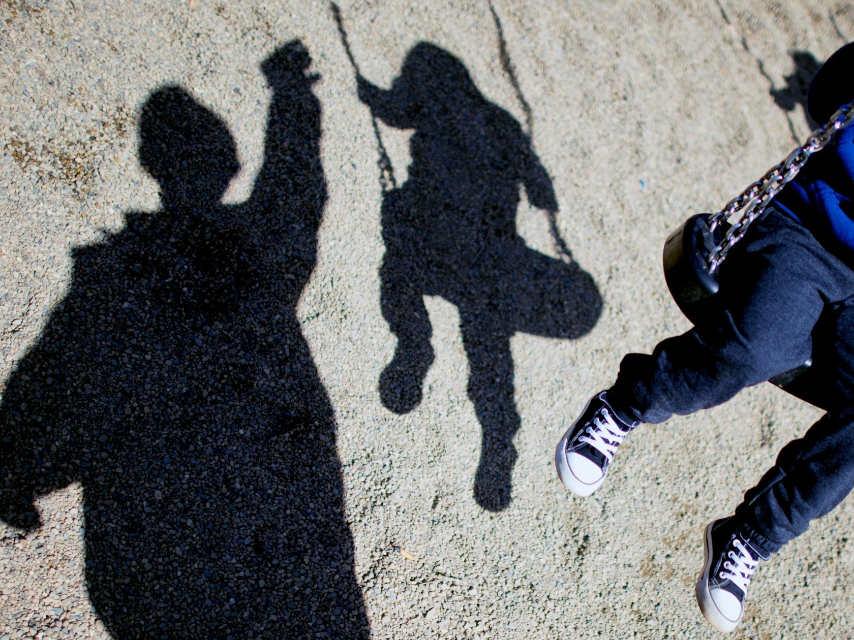 Schatten von einem Kind auf einer Schaukel und einem Erwachsenen, der dabei steht.