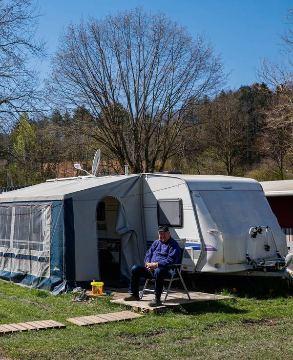 Zwei Männer sitzen in der Sonne vor einem Wohnwagen auf einem Campingplatz.
