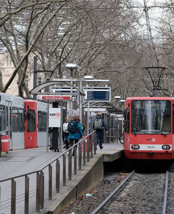 KVB-Bahn der Linie 18 hält an der Haltestelle Arnulfstraße, Menschen sind auf dem Bahnsteig zu sehen.
