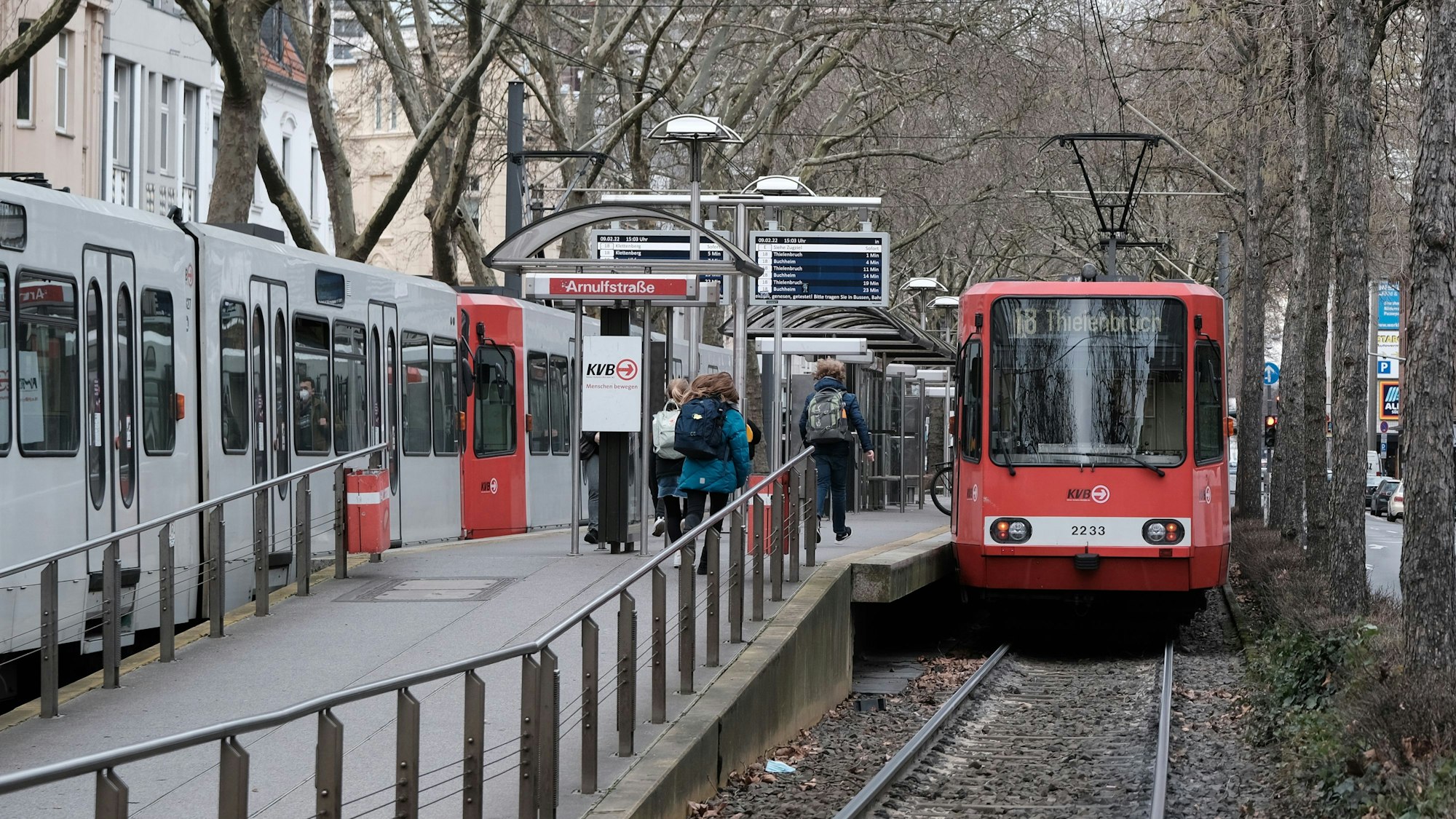 KVB-Bahn der Linie 18 hält an der Haltestelle Arnulfstraße, Menschen sind auf dem Bahnsteig zu sehen.