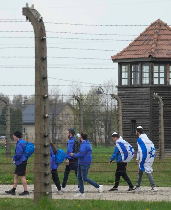 Das Symbolfoto aus dem Jahr 2022 zeigt einen Teil des Konzentrationslagers Auschwitz. Im Vordergrund befindet sich ein Stacheldrahtzaun, dahinter laufen einige Menschen in blauen Jacken und mit der israelischen Flagge.