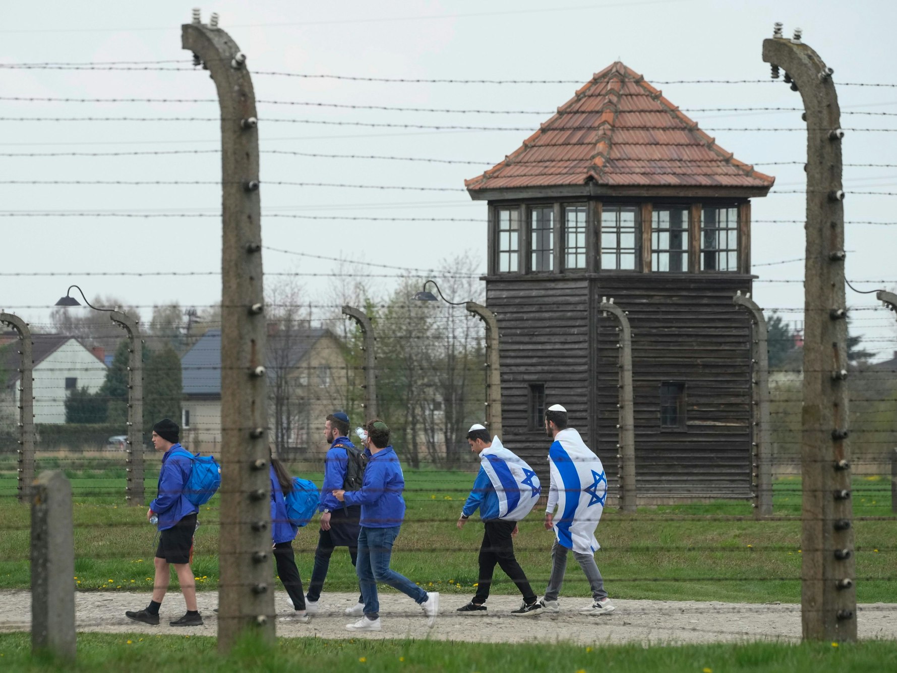 Das Symbolfoto aus dem Jahr 2022 zeigt einen Teil des Konzentrationslagers Auschwitz. Im Vordergrund befindet sich ein Stacheldrahtzaun, dahinter laufen einige Menschen in blauen Jacken und mit der israelischen Flagge.