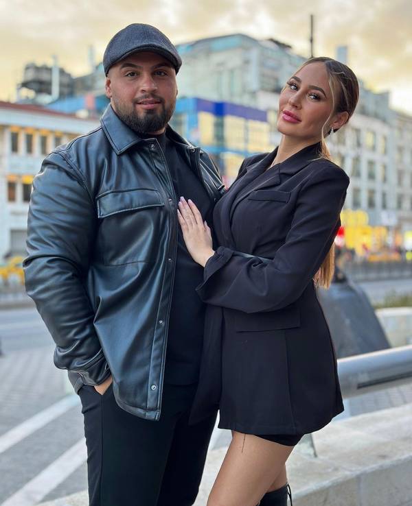 Alessia im kurzen schwarzen Kleid steht neben ihrem Freund Can. Dieser trägt ein schwarzes Outfit mit Lederjacke und Mütze.