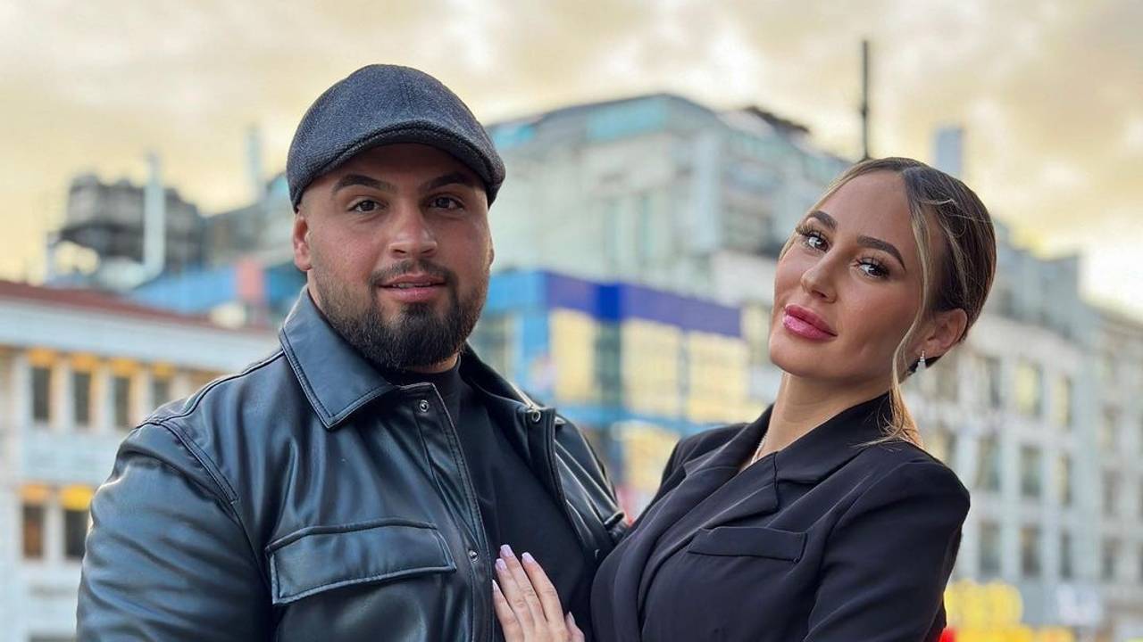Alessia im kurzen schwarzen Kleid steht neben ihrem Freund Can. Dieser trägt ein schwarzes Outfit mit Lederjacke und Mütze.