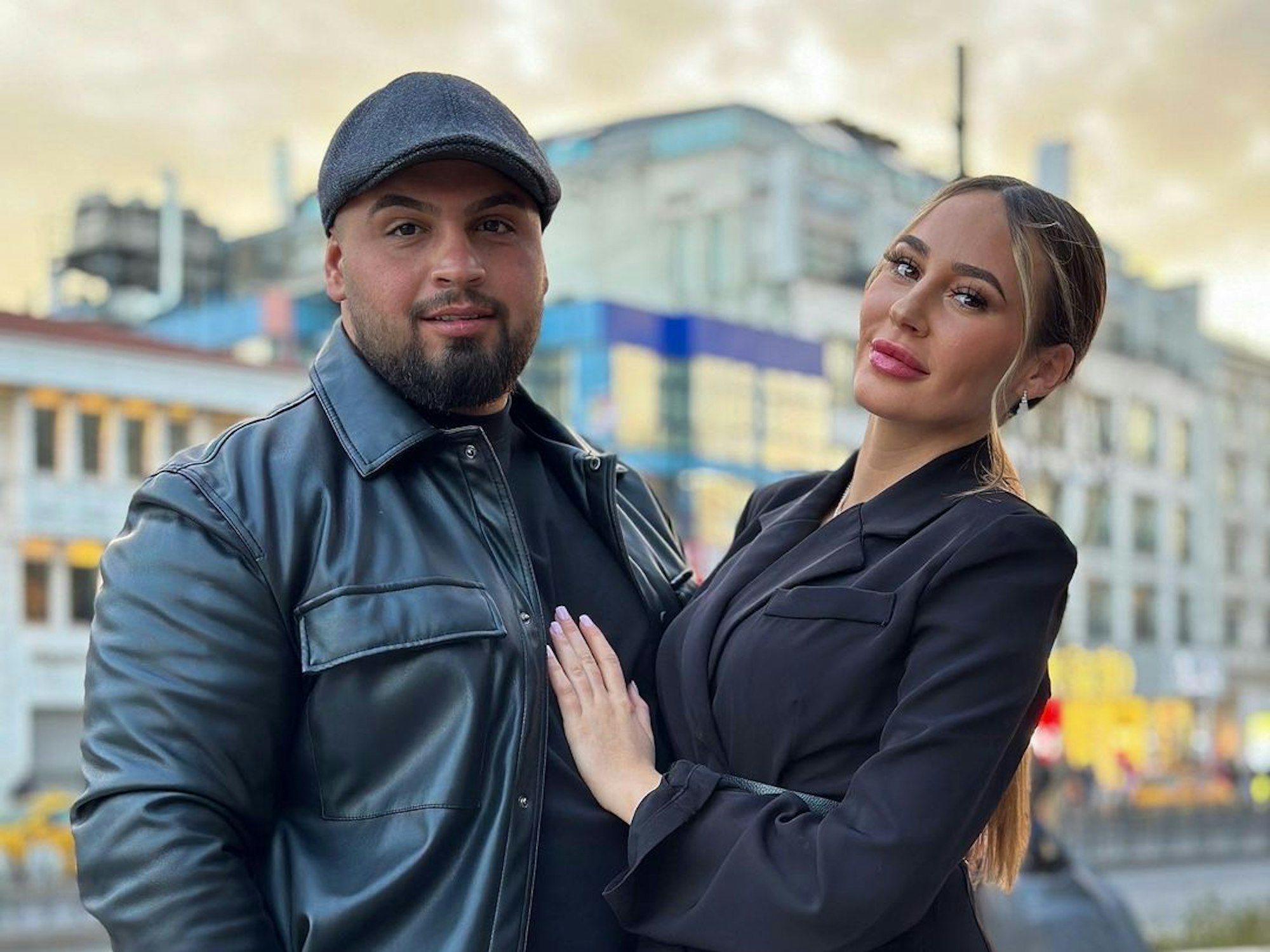 Alessia im kurzen schwarzen Kleid steht neben ihrem Freund Can. Dieser trägt ein schwarzes Outfit mit Lederjacke und Mütze.