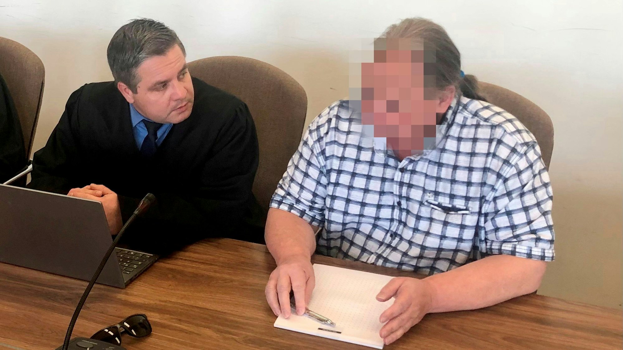 Der Angeklagte im karierten Hemd sitzt neben seinem Anwalt auf der Anklagebank.