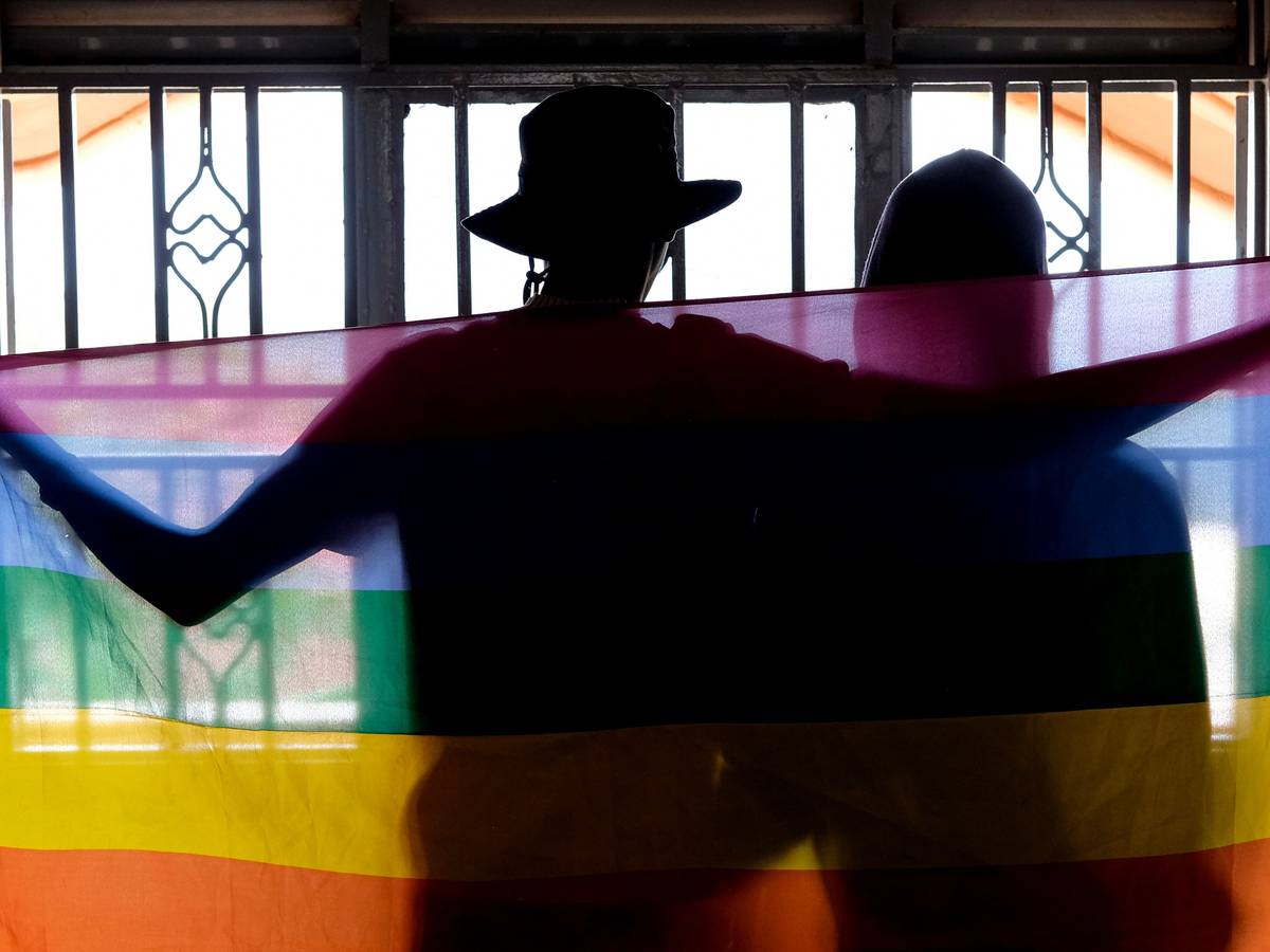 Ein schwules ugandisches Paar bedeckt sich mit einer Pride Flagge, während sie für ein Foto in Uganda posieren.