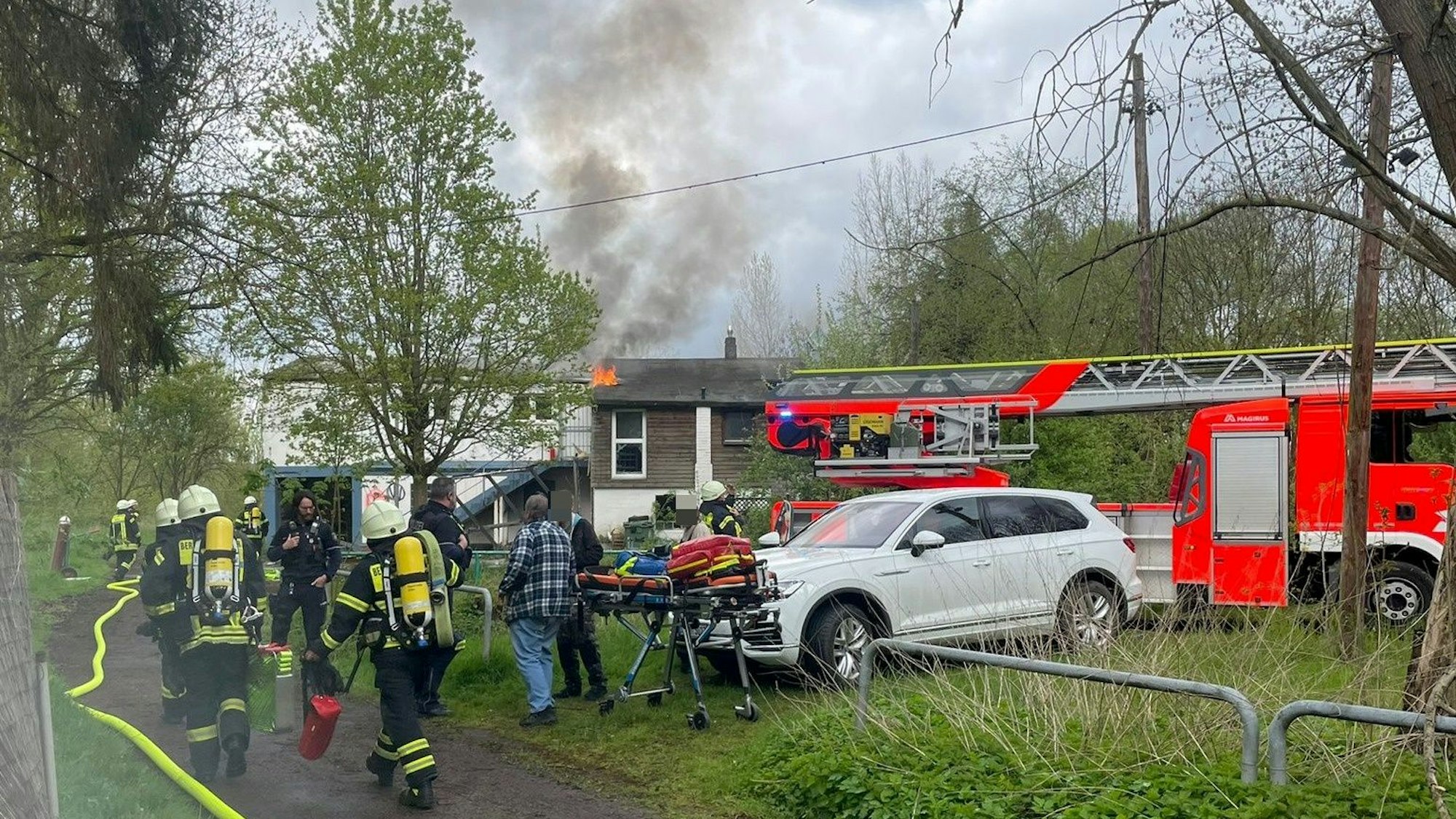 Aus einem Gebäudedach schlagen Flammen, Einsatzkräfte sind zu Fuß auf dem Weg.